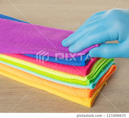 Hand in a blue glove selects a towel from a stack of bright microfiber towels for cleaning Hand in a blue glove selects a towel from a stack of bright microfiber towels for cleaning 121806635