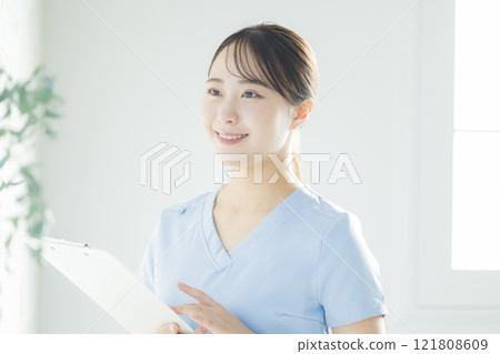 一名身穿白大褂的年輕女子，拿著病歷和活頁夾 121808609
