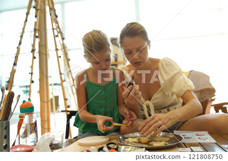 Mother and her daughter paint Halloween cookies  121808750