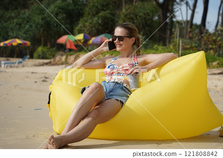 A young woman on the beach lounging on a yellow bean bag A young woman on the beach lounging on a yellow bean bag 121808842