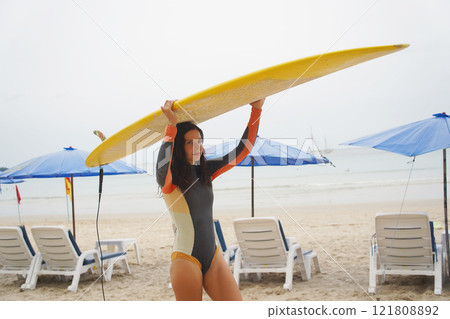 Young woman wearing tight wetsuit is going to surfboard at beautiful beach Young woman wearing tight wetsuit is going to surfboard at beautiful beach 121808892