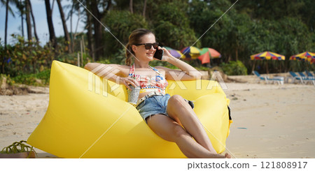 A young woman on the beach lounging on a yellow bean bag A young woman on the beach lounging on a yellow bean bag 121808917