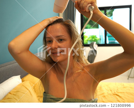 A woman is expertly styling her hair using a blow dryer and brush while in the bathroom 121808996