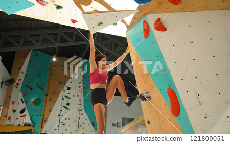 A strong female climber climbs an artificial wall with colorful grips 121809051
