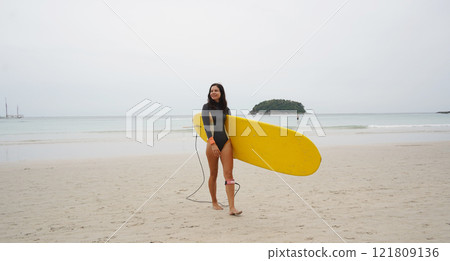 Young woman wearing tight wetsuit is going to surfboard at beautiful beach 121809136
