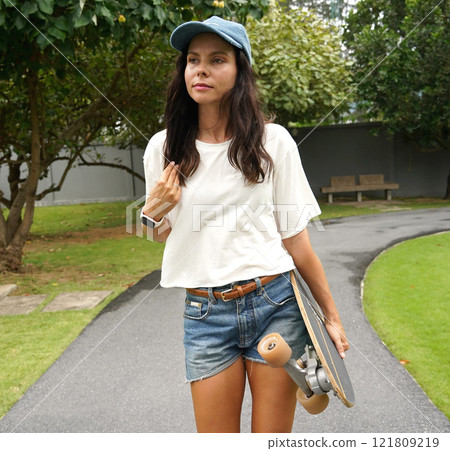 A woman is walking at the city park while carrying a skateboard in her hands 121809219