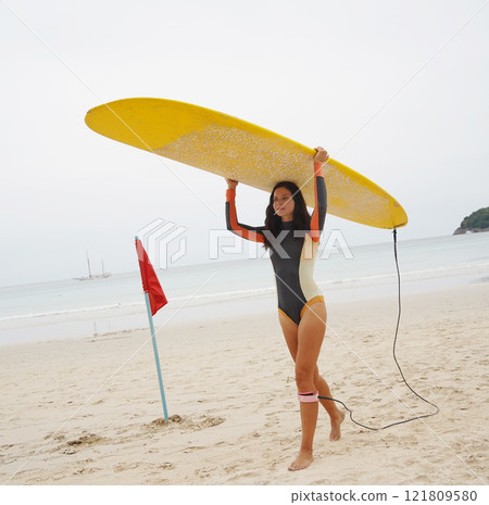 Young woman wearing tight wetsuit is going to surfboard at beautiful beach 121809580