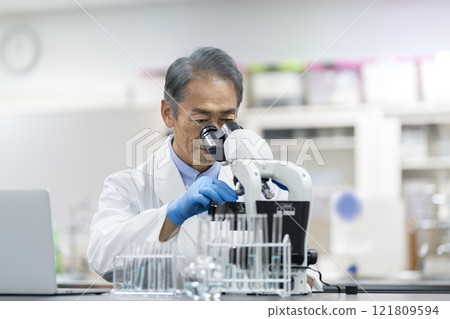 A man in a white coat working with a microscope. Image of experiment, research and development. A man in a white coat working with a microscope. Image of experiment, research and development. 121809594