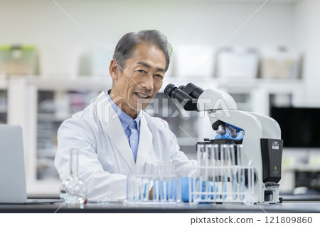 Experiment, research and development image: Man in white coat working with microscope, looking at camera, portrait 121809860