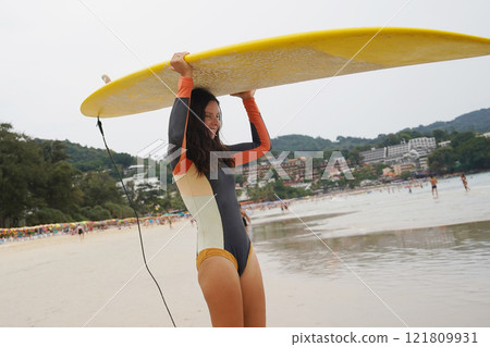 Young woman wearing tight wetsuit is going to surfboard at beautiful beach Young woman wearing tight wetsuit is going to surfboard at beautiful beach 121809931