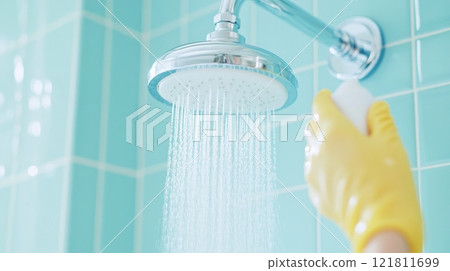 Woman cleaning chrome showerhead with spray solution on blue tiled wall in bright bathroom 121811699