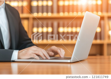 Lawyer typing on laptop in sunlit office with legal books in the background 121811749