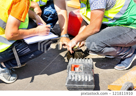 Construction crew conducts material testing during road repair in bright sunlight Construction crew conducts material testing during road repair in bright sunlight 121811910