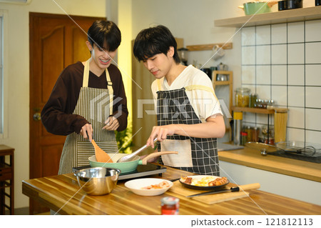 Happy gay couple preparing a delicious meal together in bright and cozy kitchen 121812113