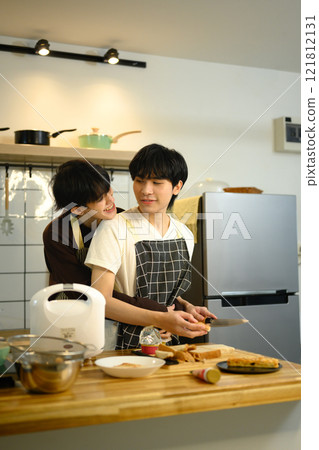 Romantic gay couple embracing while preparing a meal together in the kitchen Romantic gay couple embracing while preparing a meal together in the kitchen 121812131