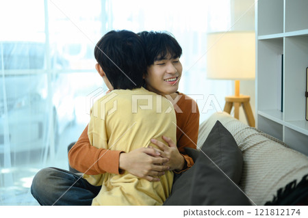Loving gay couple hugging and reassuring smile in their living room 121812174