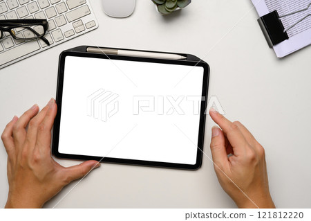 Hands holding a digital tablet with blank white screen at clean and minimalist workspace Hands holding a digital tablet with blank white screen at clean and minimalist workspace 121812220