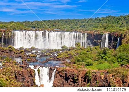 Majestic Iguacu Falls surrounded by lush greenery under a bright blue sky 121814579