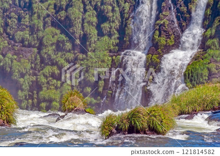 Majestic Iguacu Falls surrounded by lush greenery under a bright blue sky 121814582