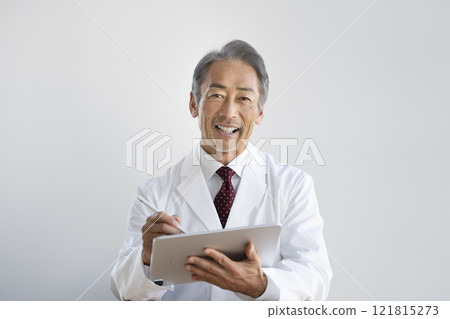 A man in a white coat talking while typing on a tablet A man in a white coat talking while typing on a tablet 121815273