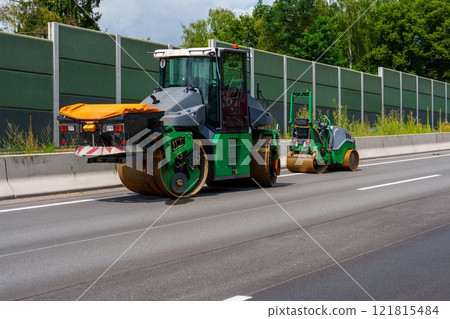 Two Green Road Construction Vehicles Paving New Asphalt on a Highway Two Green Road Construction Vehicles Paving New Asphalt on a Highway 121815484