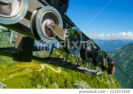 Impressive Black Cable Car Wheel Overlooking Lush Green Mountains and Scenic Landscape Views Impressive Black Cable Car Wheel Overlooking Lush Green Mountains and Scenic Landscape Views 121815489