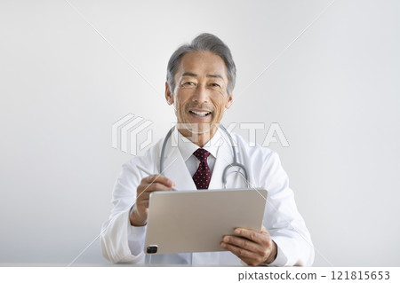 一名身穿白大褂的男子一邊在平板電腦上打字一邊說話 121815653