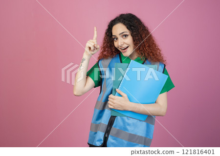 Front view of happy, pretty woman with red, curly hair standing, looking at camera, pointing up by finger. Concept of aid. Front view of happy, pretty woman with red, curly hair standing, looking at camera, pointing up by finger. Concept of aid. 121816401