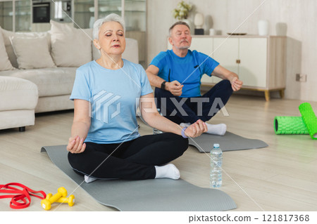 Yoga mindfulness meditation. Senior adult mature couple practicing yoga at home. Mid age old husband wife sitting in lotus pose on yoga mat meditating relaxing. Family doing breathing practice 121817368