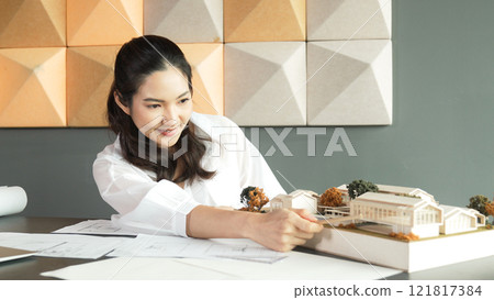 Beautiful architect measuring house model while taking a note. Manipulator. 121817384