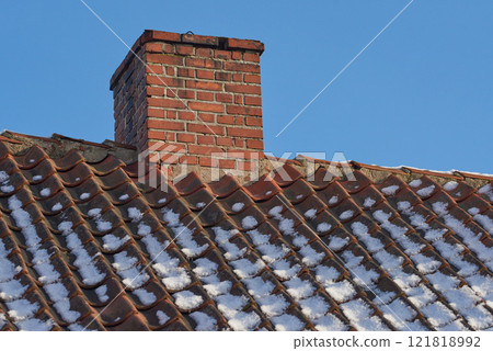 Red brick chimney designed on the roof of a snow covered residential house or building against a clear sky background. Air vent construction for the release of smoke and heat from fireplace in winter Red brick chimney designed on the roof of a snow covered residential house or building against a clear sky background. Air vent construction for the release of smoke and heat from fireplace in winter 121818992