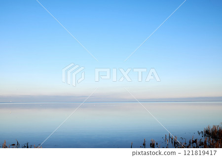 Sea at sunset with clear blue sky making a nature mirror reflection on the water with golden grey clouds on the horizon at dusk. Copy space, wallpaper background of beautiful and colorful ocean view Sea at sunset with clear blue sky making a nature mirror reflection on the water with golden grey clouds on the horizon at dusk. Copy space, wallpaper background of beautiful and colorful ocean view 121819417