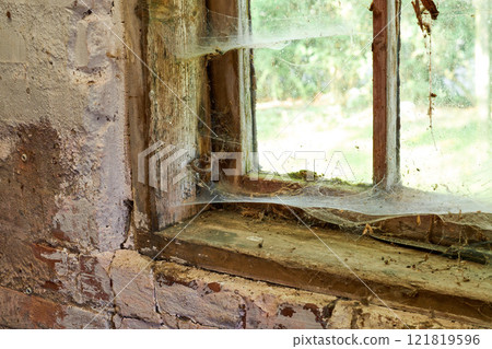 Interior view of an ancient house in need of TLC. An old window with dust and spiderwebs in an abandoned home inside. Architecture details of a windowsill frame with damaged rustic textures. Interior view of an ancient house in need of TLC. An old window with dust and spiderwebs in an abandoned home inside. Architecture details of a windowsill frame with damaged rustic textures. 121819596