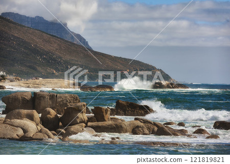 Ocean view of waves crashing against boulders or rocks in the sea in Camps Bay, Cape Town in South Africa. Relaxed and calm landscape view of the sea and mountains against a cloudy overcast sky Ocean view of waves crashing against boulders or rocks in the sea in Camps Bay, Cape Town in South Africa. Relaxed and calm landscape view of the sea and mountains against a cloudy overcast sky 121819821