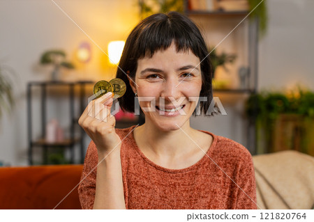 Woman stock trader holding two golden bitcoins BTC, looking at camera increasing wealth at home Woman stock trader holding two golden bitcoins BTC, looking at camera increasing wealth at home 121820764
