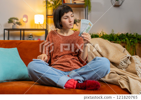 Woman counting money dollar banknotes savings earnings using smartphone calculator on sofa at home Woman counting money dollar banknotes savings earnings using smartphone calculator on sofa at home 121820765
