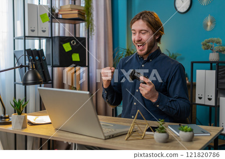 Happy freelancer business man playing video games on laptop holding controller at home office 121820786