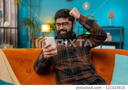 Surprised excited Indian man use smartphone reading good news amazed by online bet bid game win Surprised excited Indian man use smartphone reading good news amazed by online bet bid game win 121820810