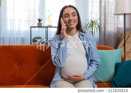 Smiling happy pregnant woman talking on smartphone stroking belly at home room pregnancy concept 121820818