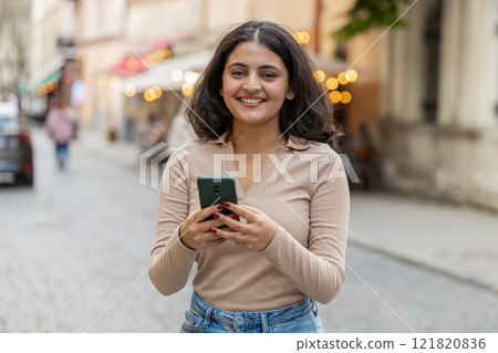 Indian woman use smartphone typing text messages browsing internet finishing work looking at camera Indian woman use smartphone typing text messages browsing internet finishing work looking at camera 121820836