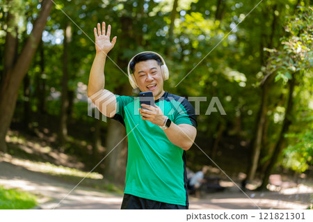 Athletic fitness Asian sport runner man walking, wearing headphones listening music from smartphone 121821301
