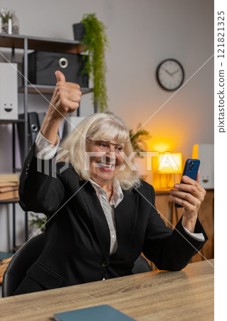 Happy mature elderly woman using smartphone typing browsing celebrating success victory at home Happy mature elderly woman using smartphone typing browsing celebrating success victory at home 121821325