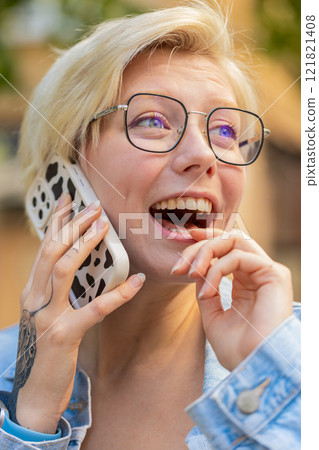 Happy young Caucasian blonde woman with short hair talking gossip on smartphone on city street Happy young Caucasian blonde woman with short hair talking gossip on smartphone on city street 121821408