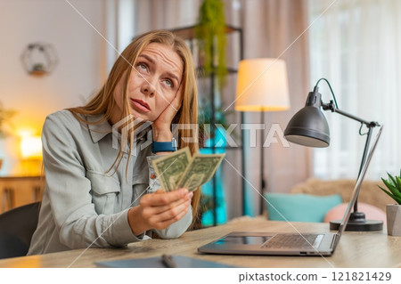 Upset Caucasian woman freelancer counting dollar cash insufficient amount of money sitting at table Upset Caucasian woman freelancer counting dollar cash insufficient amount of money sitting at table 121821429