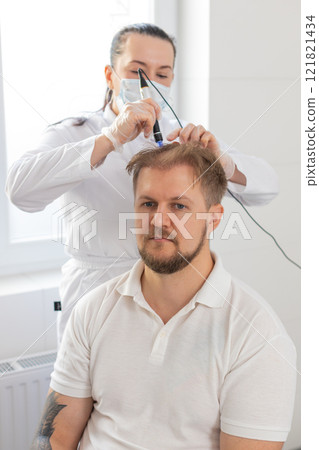Trichologist doing man improve hair growth procedure, dermapen microneedling, vitamin injections 121821434