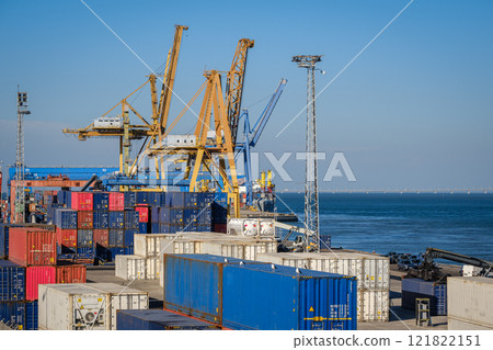 Maritime logistics and transportation scene at commercial seaport with stacked shipping containers, gantry and STS cranes, reach stackers in cargo terminal. International shipping and freight 121822151