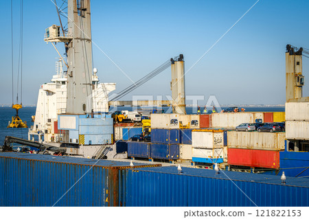 Cargo containers stacked with cars on top on bulk carrier in sea port on sunny day. Maritime logistics, transportation, commercial seaport, shipping containers in various colors, cargo handling 121822153