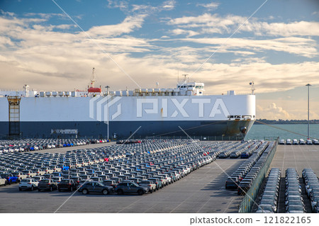 Large vehicle carrier ship known as RO-RO at port on sunny day, large parking area filled with cars. Blue sky and colorful clouds, vehicle transportation. Large vehicle carrier ship known as RO-RO at port on sunny day, large parking area filled with cars. Blue sky and colorful clouds, vehicle transportation. 121822165