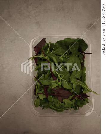 Salad mix of different types of green leaves in a plastic container on a gray background Salad mix of different types of green leaves in a plastic container on a gray background 121822280
