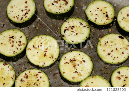 A seasoned sliced courgette with salt and herbs waiting to be cooked in the oven close up raw A seasoned sliced courgette with salt and herbs waiting to be cooked in the oven close up raw 121822503